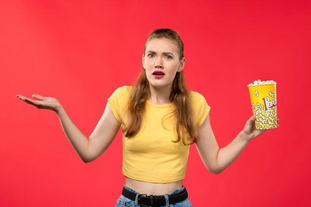 爆米花正面图年轻女性在电影院拿着爆米花在红墙电影院吃小吃的女性趣味电影电影院剧院年轻人