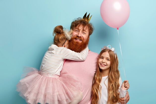 孩子孩子们 节日的概念快乐的爸爸带着姜黄色的胡子在聚会上逗女儿们开心 手上抱着小女儿 大女儿站在气球旁边 庆祝生日或儿童节积极真实快乐
