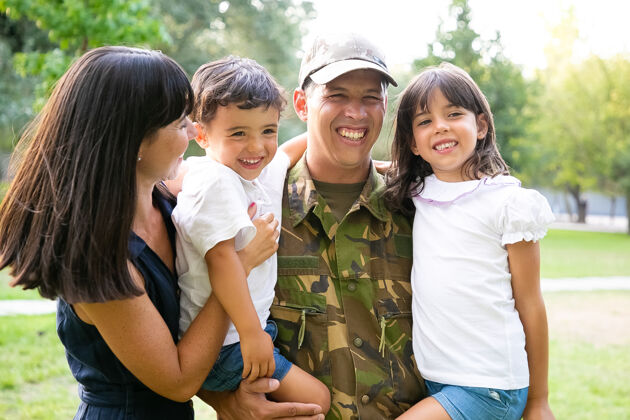 镜头快乐的军人和他的家人合影 抱着孩子 他的妻子抱着他们笑中镜头家庭团聚或回家的概念军人笑父母
