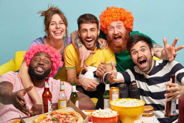 快乐各种各样的球迷朋友用爆米花 披萨和饮料庆祝他们最喜爱的球队的成功 坐在沙发上 在电视前度过周日的夜晚 隔着蓝色的墙家庭影院娱乐球迷积极