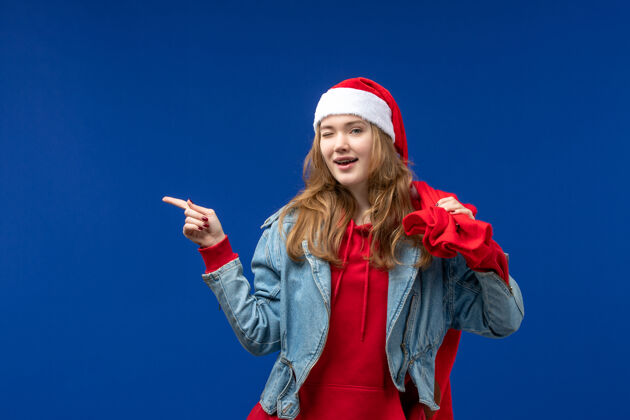 颜色正面图：年轻女性拎着装满礼物的袋子 蓝色的地板上 圣诞节头发肖像年轻