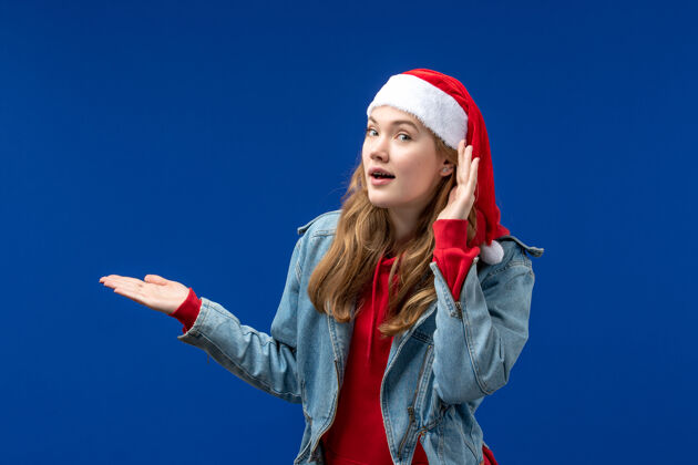 漂亮正面图：戴着红色圣诞帽的年轻女性 背景是蓝色的圣诞情感色彩女性蓝色微笑