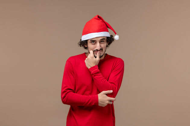 快乐正面图：一个表情混乱的年轻人在棕色背景下过圣诞节节日工作人