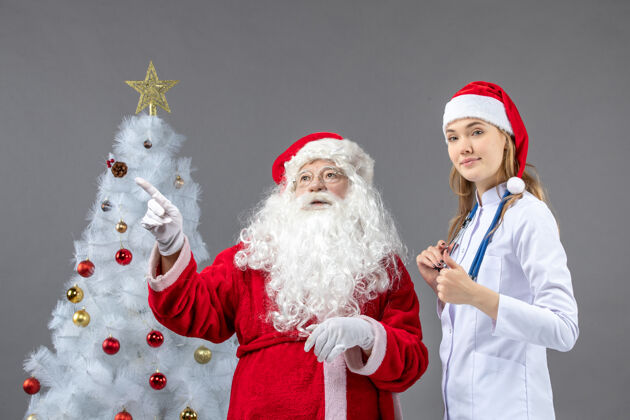 圣诞圣诞老人和年轻女医生在灰色墙壁上的正视图圣诞快乐男人快乐