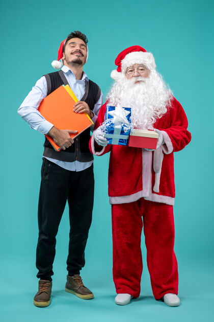 圣诞老人圣诞老人与年轻男性和礼物在蓝色墙上的正面视图服装人们节日