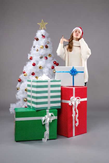 购物年轻的女性在灰色的礼物圣诞老人圣诞树帽子