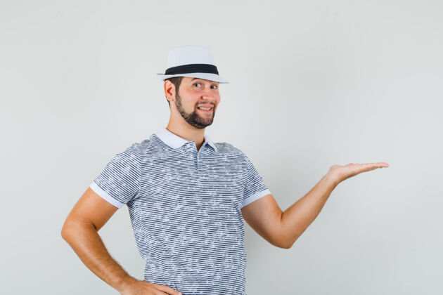 工作室年轻人穿着条纹t恤 戴着帽子 看上去很高兴 欢迎或展示某物正面视图时尚表情人