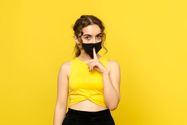 人黄墙上戴着面具的年轻女子的正视图成人流行时尚