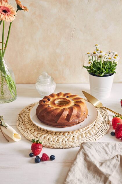 鲜花在白色背景的白色桌子上 一个带水果的环形蛋糕的垂直镜头戒指聚会糕点