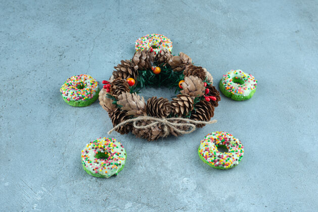 洒五个甜甜圈环绕在大理石上的松果花环上可口糖糖果