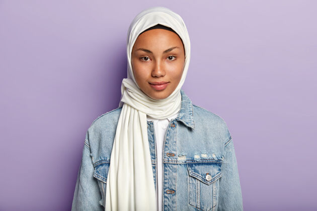 模特美丽的女人 健康的深色皮肤 戴着白色头巾 穿着牛仔夹克 目光直视 隔离在紫色的墙壁上宗教女性有自然美种族观念东方严肃摆姿势