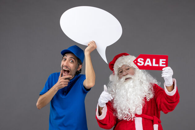庆祝圣诞老人与男信使手持白色标志和灰色墙上的销售横幅的正面视图十二月圣诞老人举行