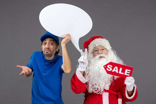 前面圣诞老人与男信使手持白色标志和灰色墙上的销售横幅的正面视图成人举行节日