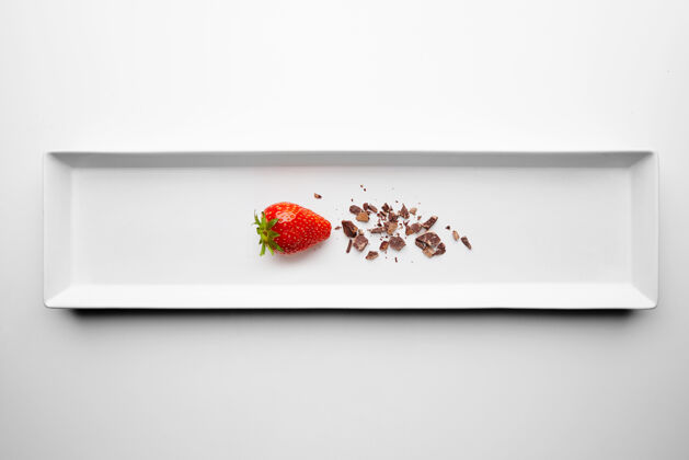 黑熟透的新鲜草莓接近巧克力屑呈现在餐厅的中心矩形陶瓷盘上 在白色背景上独立提供工作室美食巧克力浸泡