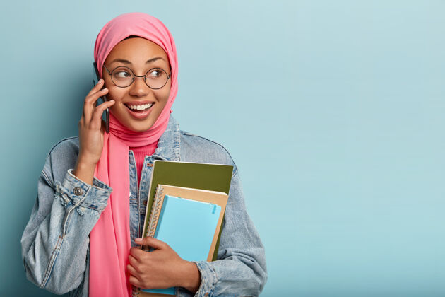 摄影棚拍摄的快乐积极的女性有伊斯兰宗教观点 在智能手机上讨论一些事情一旁墙壁持有