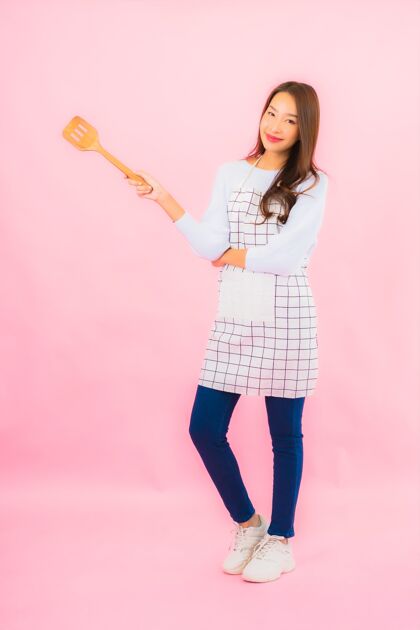 新鲜肖像美丽的亚洲年轻女子在厨房穿着围裙在粉红色的隔离墙上制服认可厨师