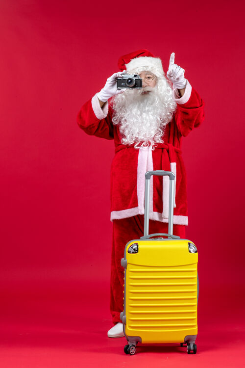 舞者红墙上带黄包的圣诞老人用相机拍照的正面图圣诞快乐快乐节日