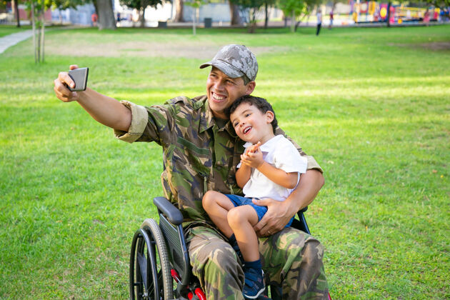 父亲快乐的残疾军人爸爸和他的小儿子一起在公园里自拍男孩坐在爸爸的膝盖上退伍军人或残疾概念父母椅子伪装