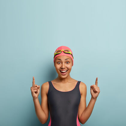 指向积极的女人喜欢水上运动 穿着黑色泳衣 戴泳帽和护目镜 在自由空间上得分 为潜水做广告 为比赛做准备运动和推广概念苗条微笑女运动员