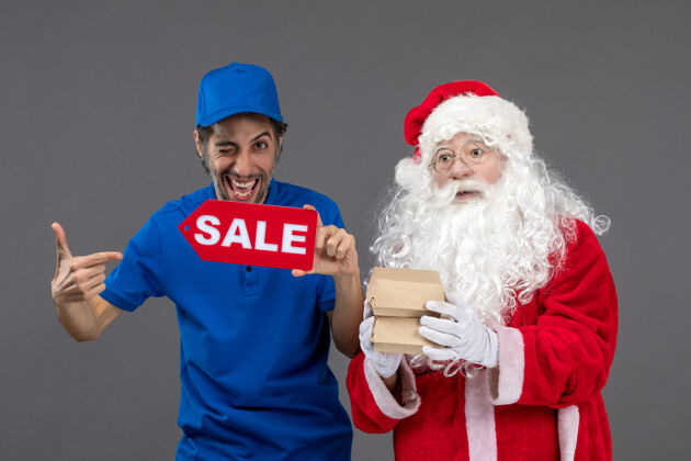 圣诞老人圣诞老人的正面图 男信使手持销售横幅 灰色墙上有食品包装圣诞老人节日食品