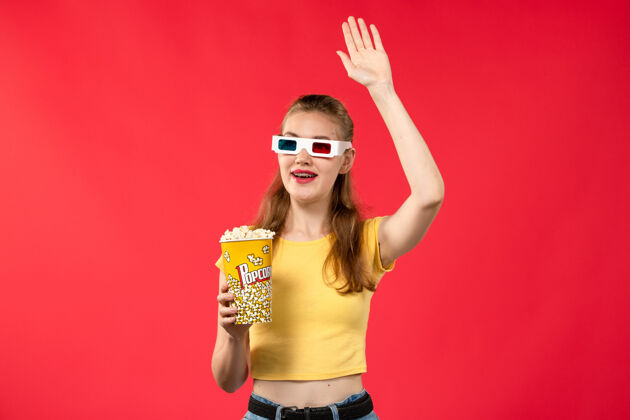 电影院正面图年轻女性在电影院拿着爆米花包在d太阳镜上看红墙电影成人电影年轻女性