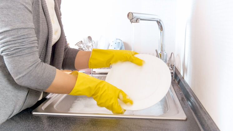 家用你这个戴着橡胶手套的家庭主妇在厨房的水槽里洗碗玻璃海绵日常
