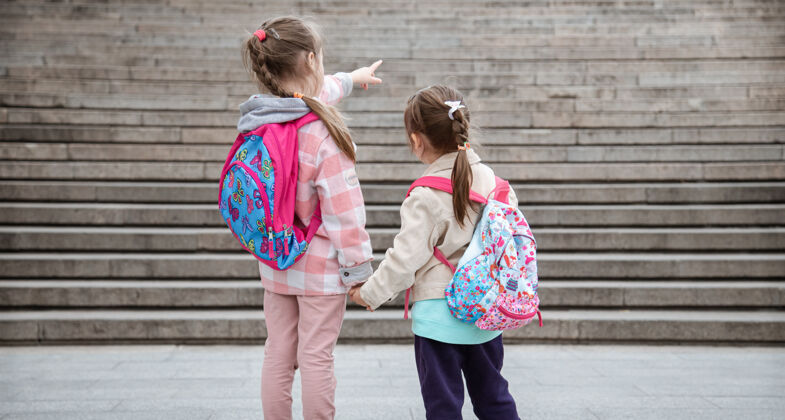 一起两个背着漂亮背包的小女孩手牵手一起上学童年友谊的概念友谊小学生女生