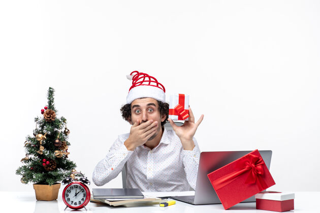 提高圣诞节心情惊讶的商人与圣诞老人的帽子举起他的礼物 并关闭他的嘴白色背景男性商务人士结束