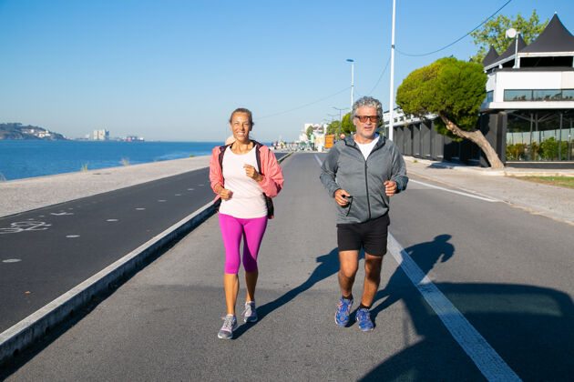 慢跑快乐的成年夫妇沿着河岸慢跑白发男女穿着运动服 在户外跑步活动和年龄观念老年人活动头发