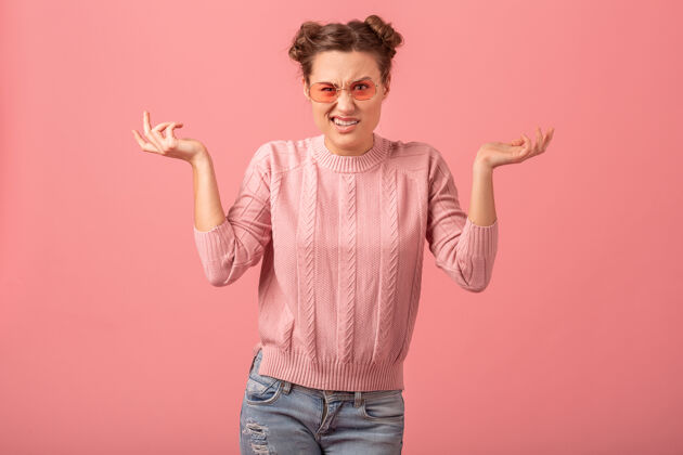表情年轻漂亮有趣的女人有一个问题 感觉压力 手举着粉红色毛衣和太阳镜隔离在粉红色的工作室背景悲伤眼镜摆姿势