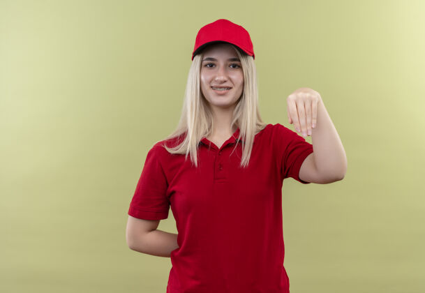 手势微笑的小女孩 戴着红色t恤 戴着帽子 在与世隔绝的绿色背景上展示着“接受”的姿态绿色穿着采取