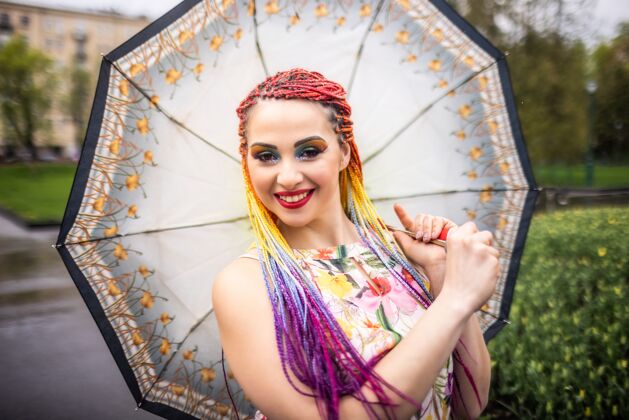 天气带着不寻常的闪光妆容的女孩 带着五彩的人造辫子 穿着印花连衣裙打着伞到处转雨伞表达笑