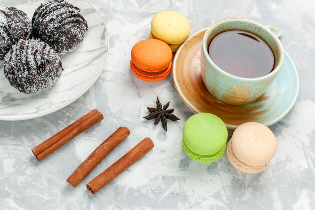 麦卡龙前视图一杯茶 麦卡龙巧克力蛋糕和肉桂 在白色桌子上烤蛋糕饼干糖甜派生的早餐勺子