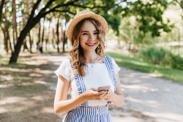 成人浪漫的女孩戴着帽子 穿着白色t恤 对大自然微笑可爱的金发女人喜欢在公园散步微笑年轻金发