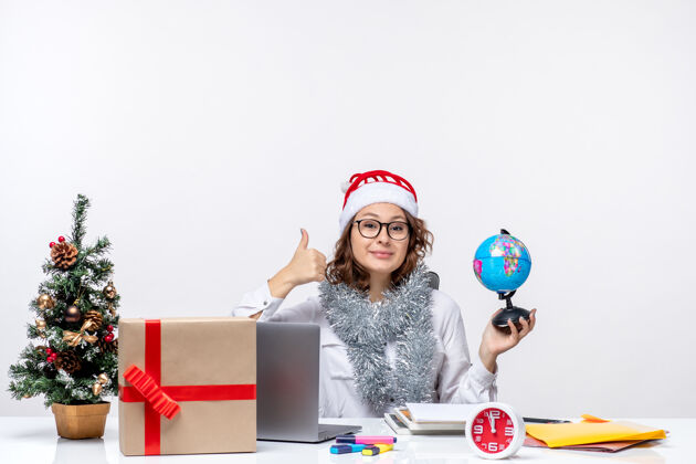 拇指向上正面图年轻的女工坐在她拿地球仪的地方前 在白色的地板上办公 在圣诞节上班的女士坐着女士办公室