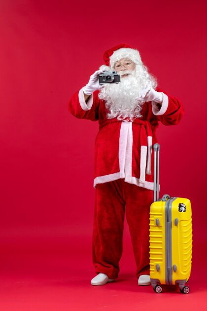 行李前视图的圣诞老人与黄色袋拍照与相机上的红墙快乐前面男人