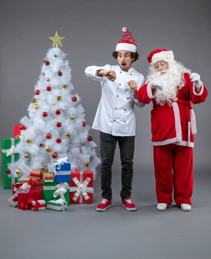 雪人圣诞老人和男厨师在灰色墙上围着圣诞礼物的正视图快乐前面帽子