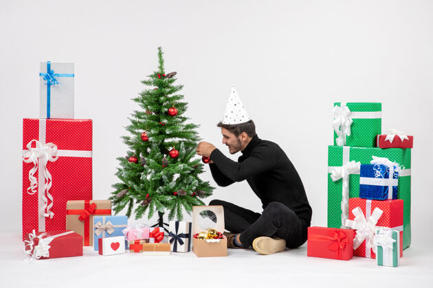 坐年轻人围坐在节日礼物装饰白色墙上的小树的前视图装饰冬青圣诞快乐
