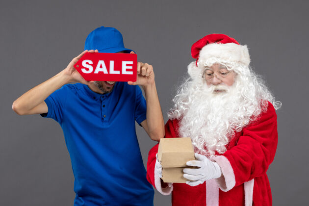 圣诞老人圣诞老人的正面图 男性信使手持销售横幅 灰色墙上有食品包装正面男人人
