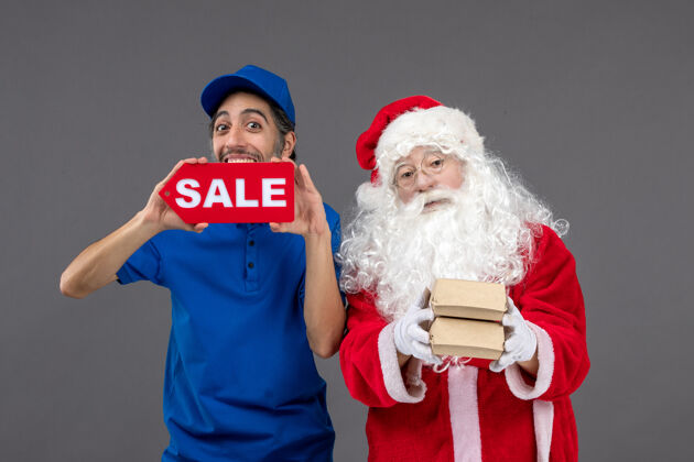 庆祝圣诞老人的正面图 男信使手持销售横幅 灰色墙上有食品包装男性包裹圣诞老人