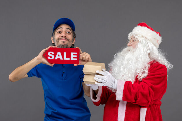 庆祝圣诞老人的正面图 男信使手持销售横幅 灰色墙上有食品包装圣诞圣诞老人举行