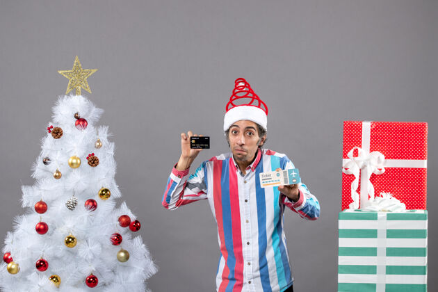 肖像前视图体贴的男人拿着卡片和旅行票围着圣诞树和礼物人灰色持有