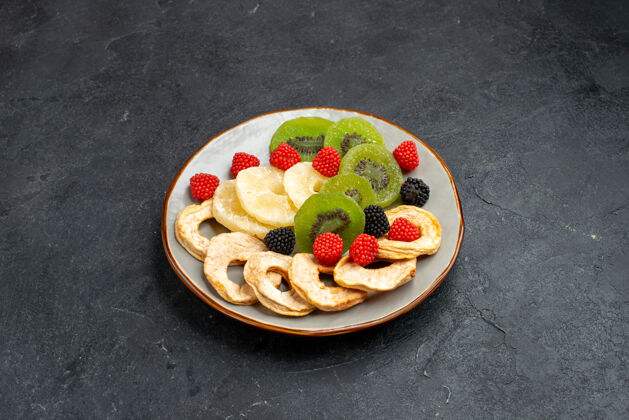 菠萝前视图干菠萝环与干猕猴桃和苹果暗灰色表面水果干葡萄干甜糖果餐糖果水果