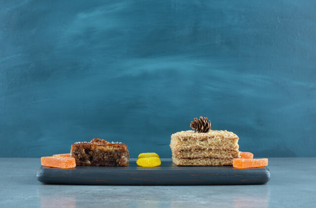 甜点在大理石表面的海军蓝板上放一块蛋糕 烤面包和一些果冻糖果甜点美味蛋糕