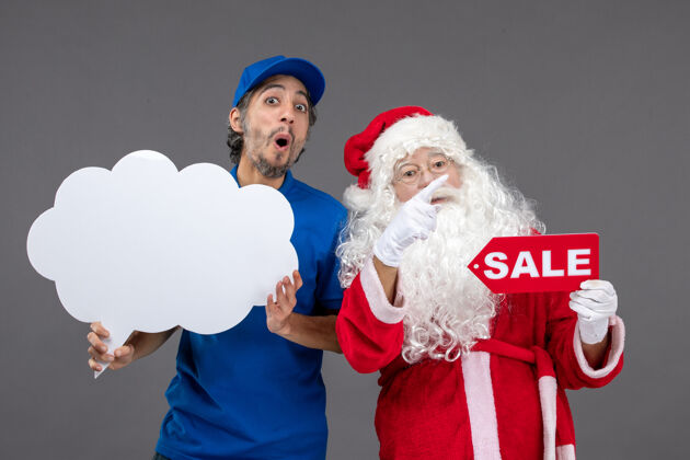 男圣诞老人的正面图 男信使手持白云招牌 在灰色墙上出售圣诞快乐快递人