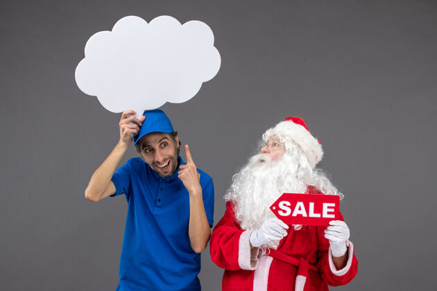 圣诞快乐圣诞老人的正面图 男信使手持白云招牌 在灰色墙上出售人圣诞云
