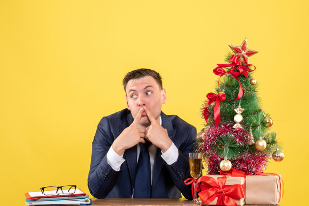 音乐家坐在圣诞树旁桌子旁的一个好奇的人 把礼物放在黄色的桌子上树好奇的人歌手
