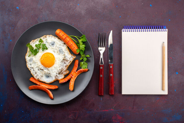 盘子顶视图炒鸡蛋与绿色和香肠内板与记事本在黑暗的表面桌子菜炒的