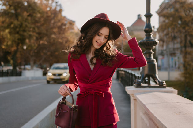 穿着酷酷靓丽的时尚女人穿着紫色西装走在城市街头 春夏秋冬时节时尚潮流戴着帽子 手拿钱包套装夹克深色