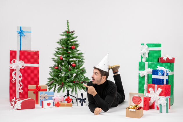 十二月年轻人躺在白色墙上的节日礼物周围的正面视图节日礼物模型